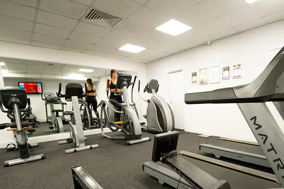 Gym equipment in front of a mirror with a lady using a cross trainer machine
